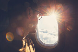 Man looks out of airplane window towards the sun
