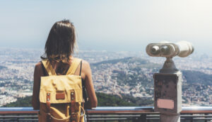 girl with backpack overlooking Barcelona, Spain from observation deck with tourist binoculars.