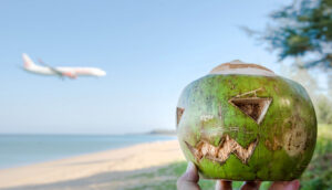 Coconut jack o'lantern on beach for halloween with airplane in background