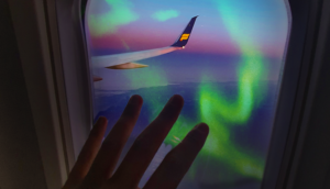hand on the window of icelandair plane with northern lights outside
