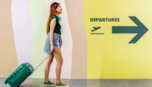 woman walking through departures terminal airport rolling luggage