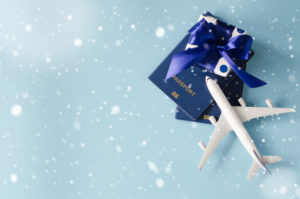 Two passports, a small wrapped gift, and a toy airplane on a blue background with snow in the foreground