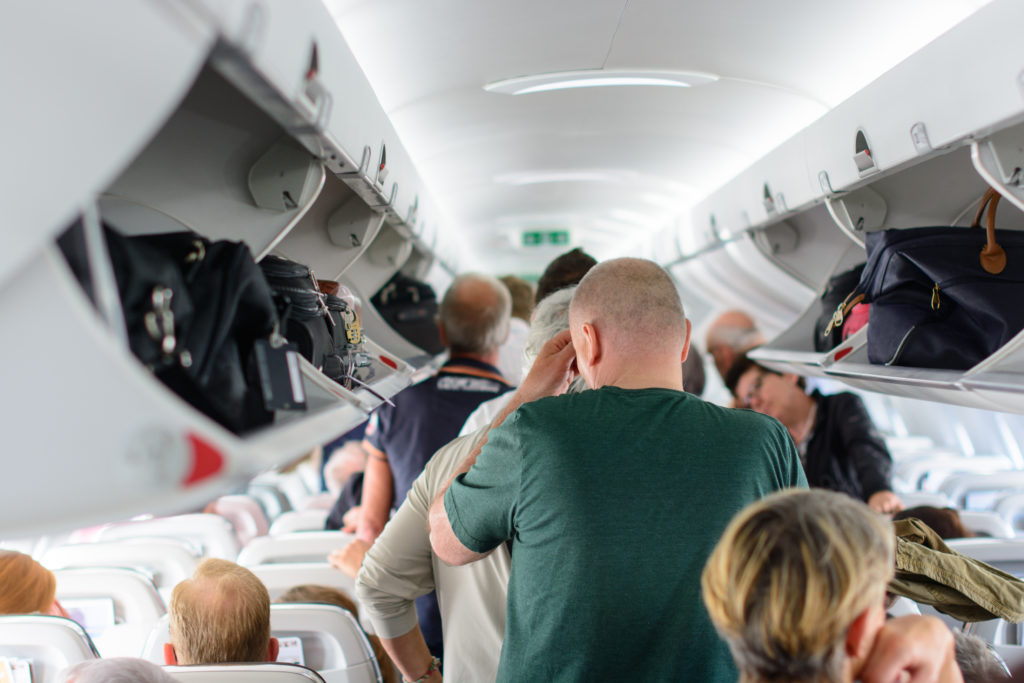 Airplane aisle crowded with passengers loading luggage into overhead bins