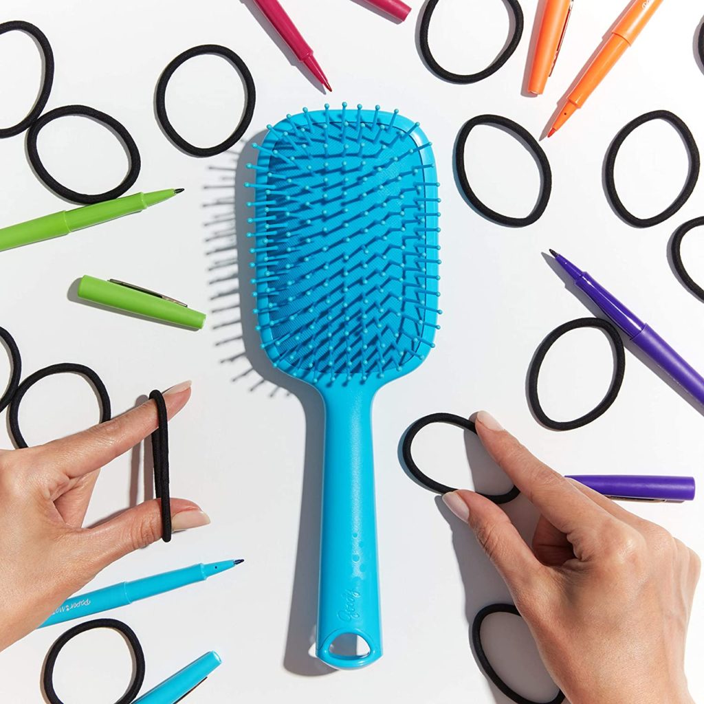 Hair ties and colorful markers surrounding a blue hair brush
