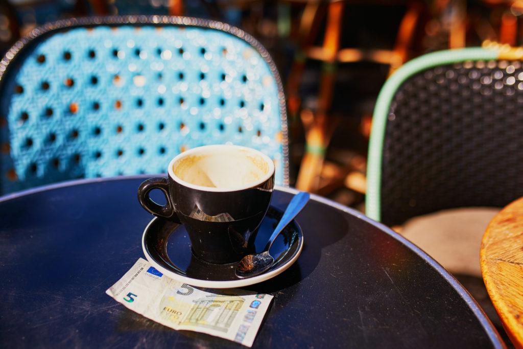A tip in euros left beside an empty coffee mug at an outdoor table