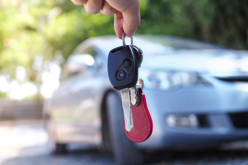 A pair of keys in the foreground dangled in front of a blurry white car