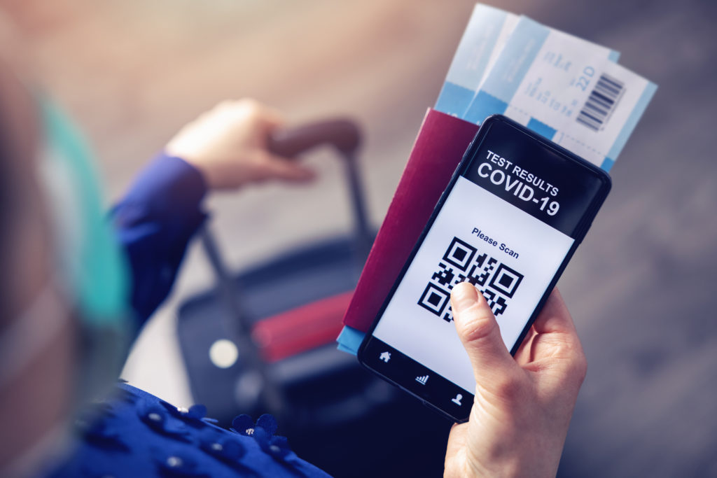 Person at airport holding luggage, a passport, boarding passes, and a phone showing COVID-19 test results