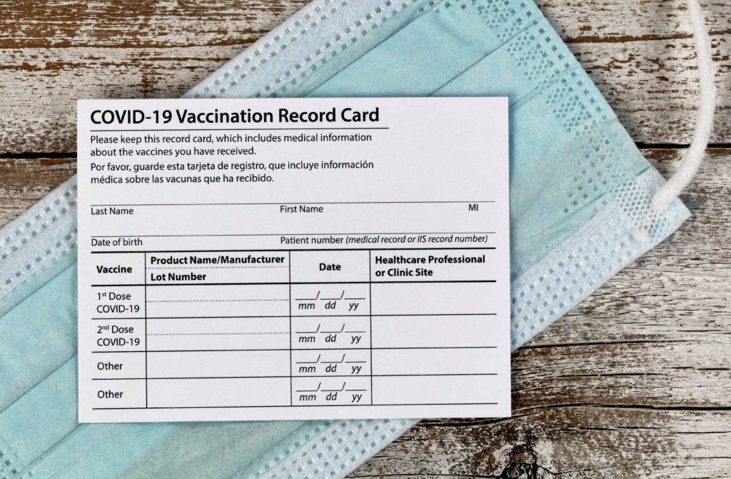 COVID-19 vaccination card and face mask on a wooden background