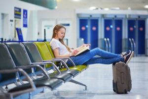 Woman in airport terminal resting feet on carry-on luggage