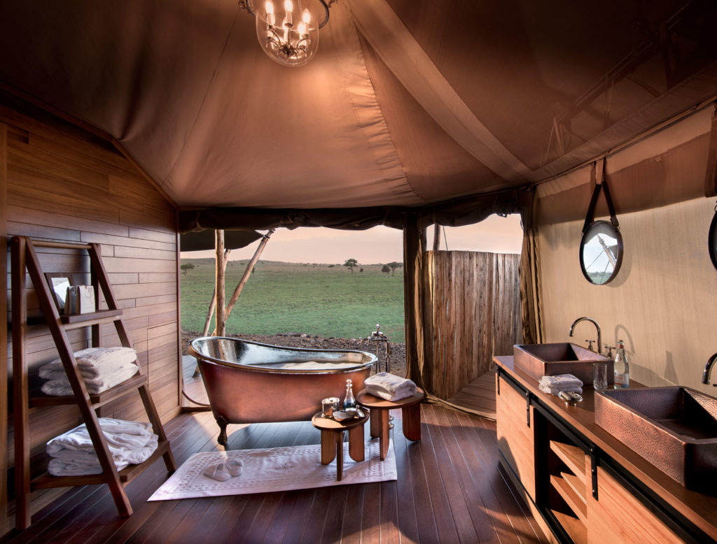 A free-standing bathtub in a luxurious tent with wooden floors and fixtures overlooking the Serengeti