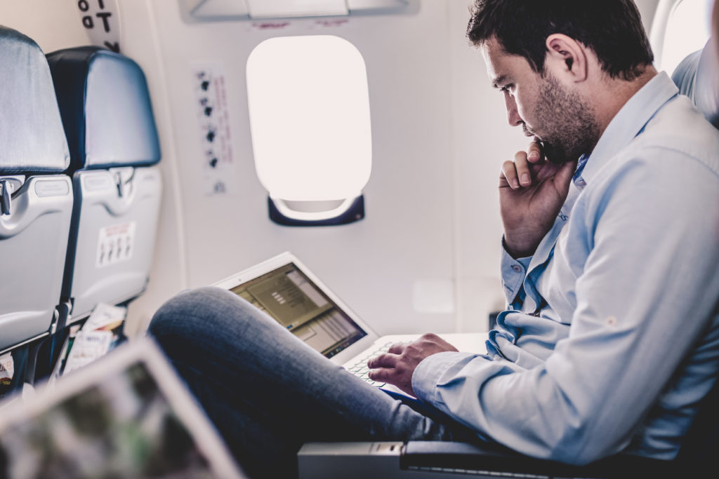 Man working on laptop in the middle seat of an airplane row