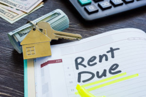 The words "rent due" written on a planner notebook surrounded by house keys, a calculator, and cash