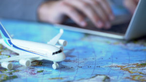 Model airplane on a world map with a person in the background booking a flight on a laptop