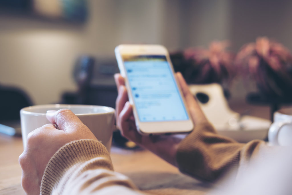 Woman using social media on phone in one hand and holding a mug in the other hand