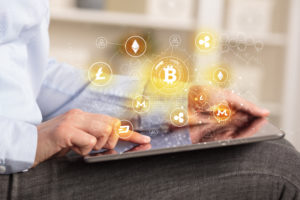 Person using tablet with graphics illustrating cryptocurrency displayed above the screen