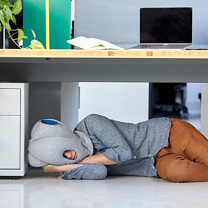 Person taking a nap underneath a desk with the Ostrich Pillow