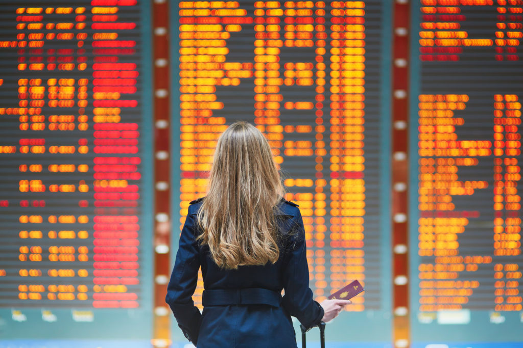Woman watching the departures board at an airport with a suitcase