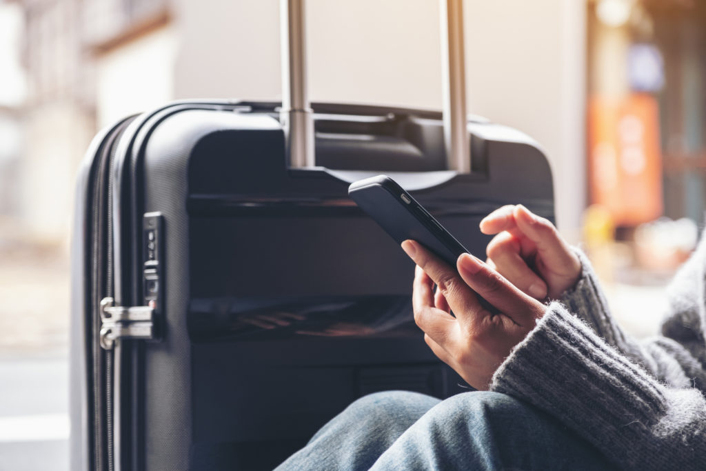 Close-up of person using smartphone next to rolling luggage