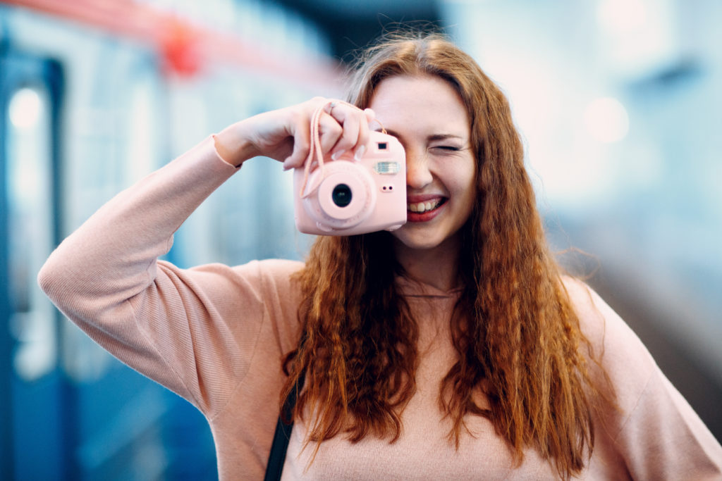 Woman with long red hair snapping a photo with a pink instant camera