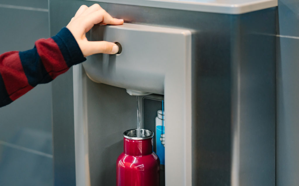 Person filling up a reusable water bottle from a water station