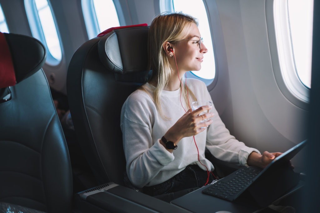 Woman drinking a glass of water while working on her laptop on an airplane