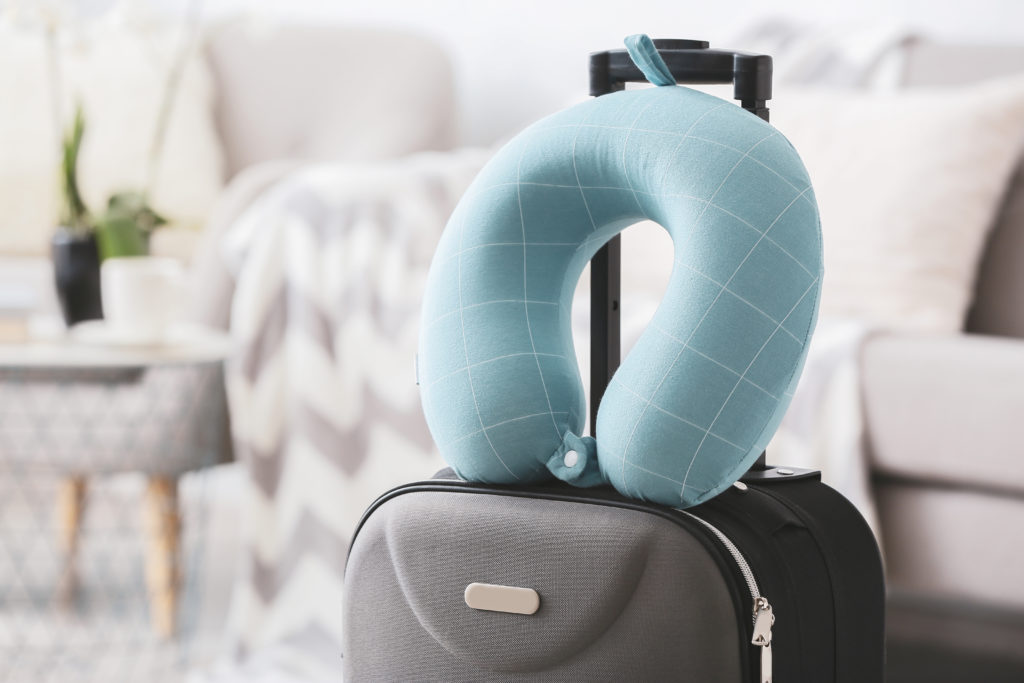 Travel pillow hooked to the retractable handle of a suitcase in a light colored living room