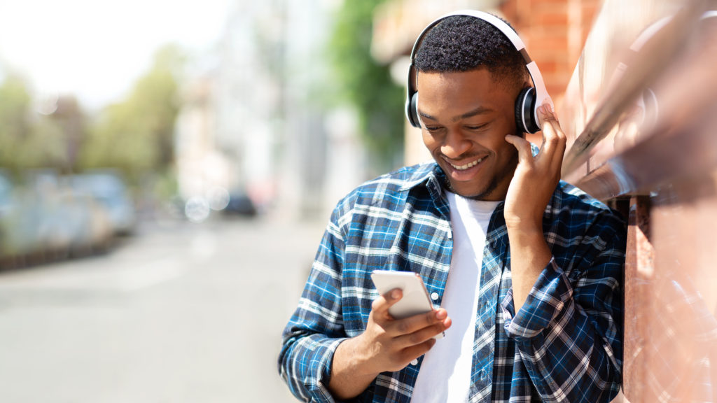 Person leaning against a brick wall and listening to music on his phone