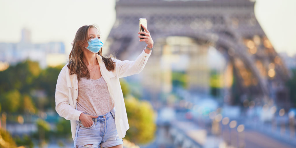 Woman wearing a face mask taking a selfie in front of the Eiffel Tower