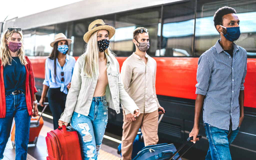 Group of friends wearing face masks, carrying luggage and walking next to a train