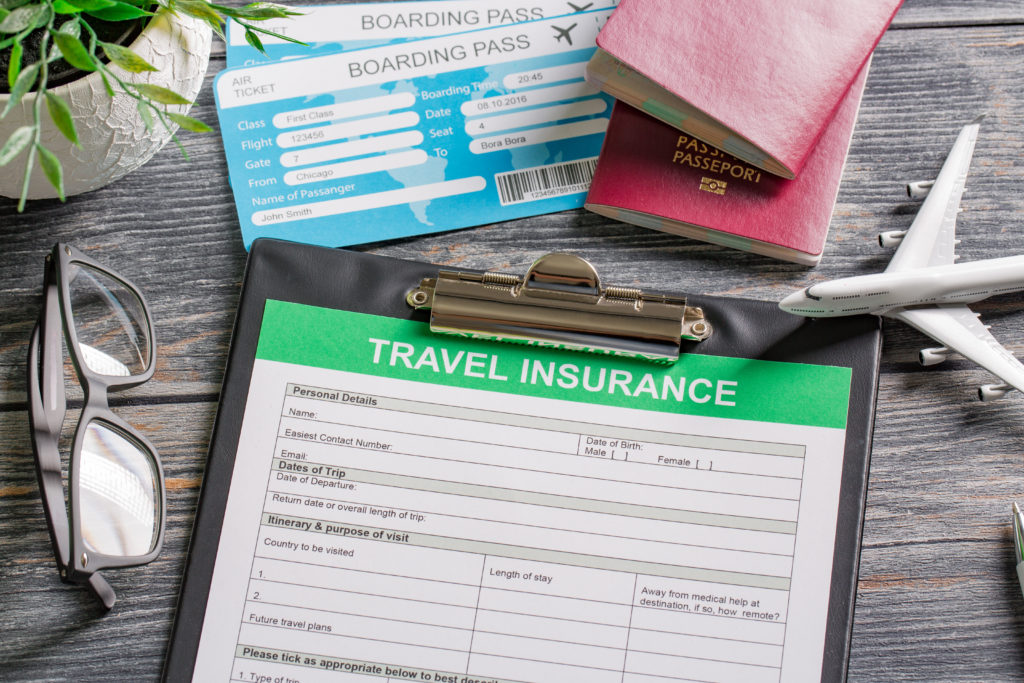 Travel insurance papers on a desk with boarding passes, passports, and glasses