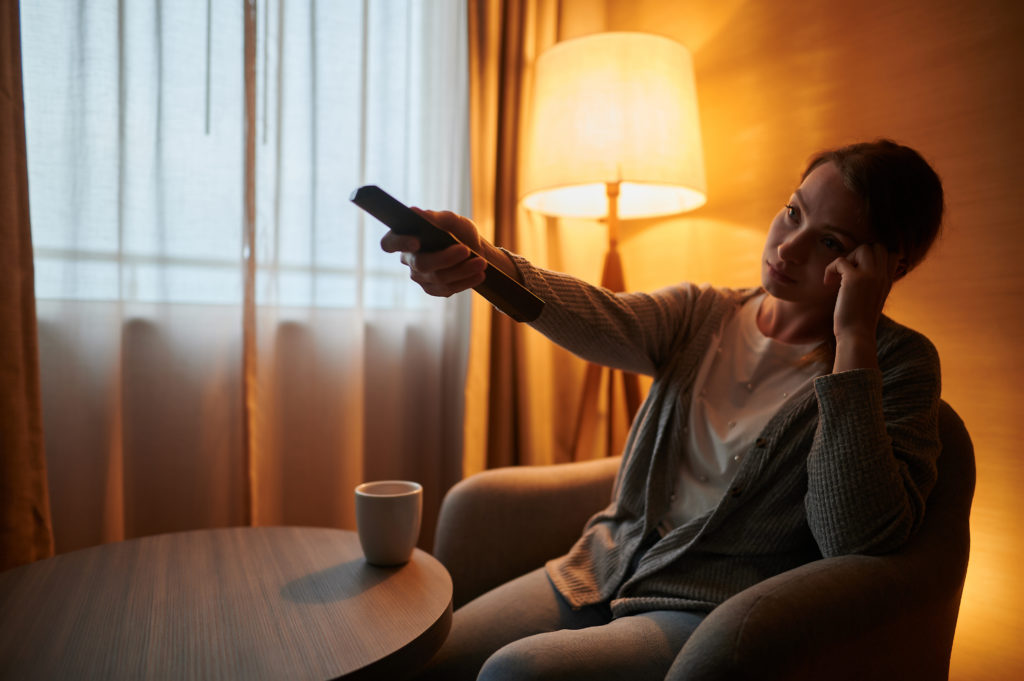 Bored looking woman flipping through TV channels in hotel room