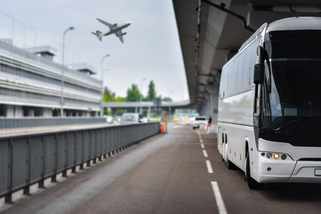 Large bus waiting at airport with plane taking off in background